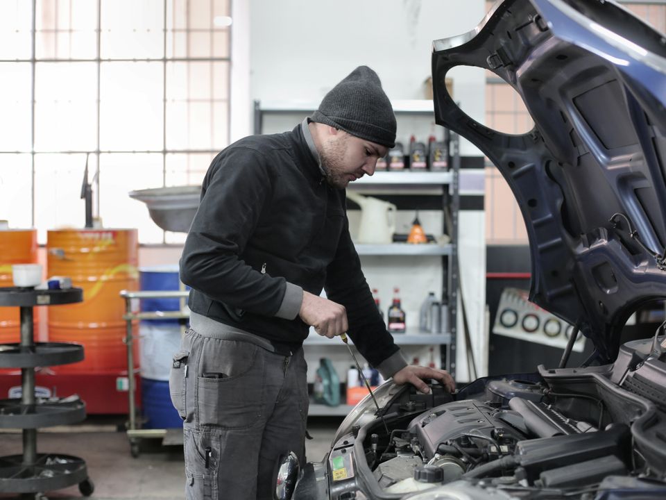 Mechaniker mit Mütze arbeitet im Motorraum eines Autos